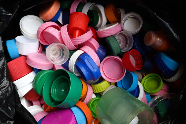 grupo de tampas de garrafa multicoloridas em saco de plástico preto, pronto para reciclagem vista superior
  - Foto, Imagem