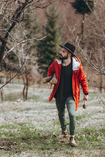 Hipster with beard,  Man in hat and warm jacket chopping and preparing firewood for picnic - Fotoğraf, Görsel