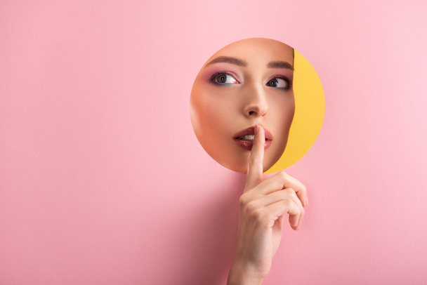 muotokuva kaunis nainen kiiltävä meikki vaaleanpunainen paperi pyöreä reikä osoittaa shh merkki eristetty keltainen - Valokuva, kuva