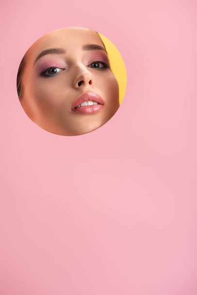 portrait of beautiful woman with shiny makeup in pink paper round hole isolated on yellow - Zdjęcie, obraz