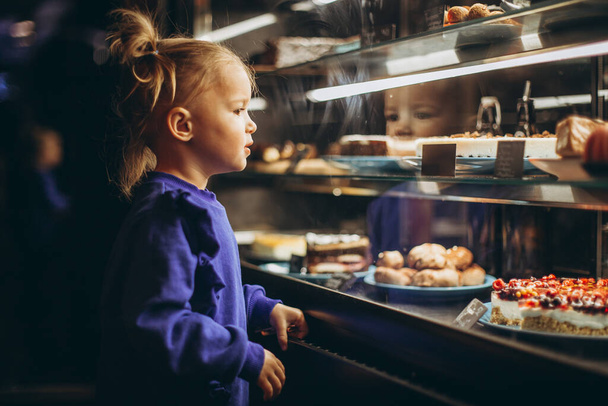 little pretty girl chooses pastries in a cafe. a child next to a showcase with goods - Foto, immagini