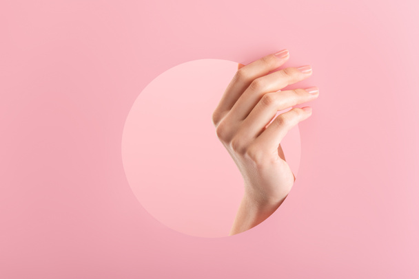 cropped view of female hand in paper round hole isolated on pink - Foto, immagini