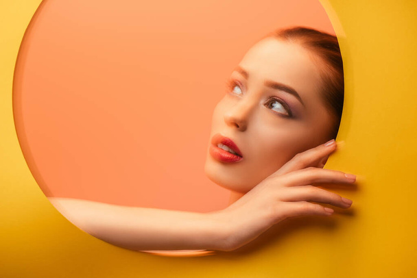 blurred image of beautiful woman in yellow paper circle hole looking away - Фото, изображение