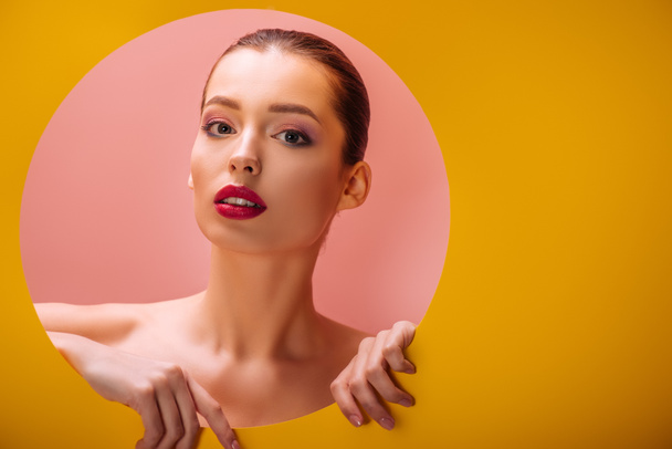 naked beautiful woman with crimson lips in yellow paper circle hole on pink background - Φωτογραφία, εικόνα