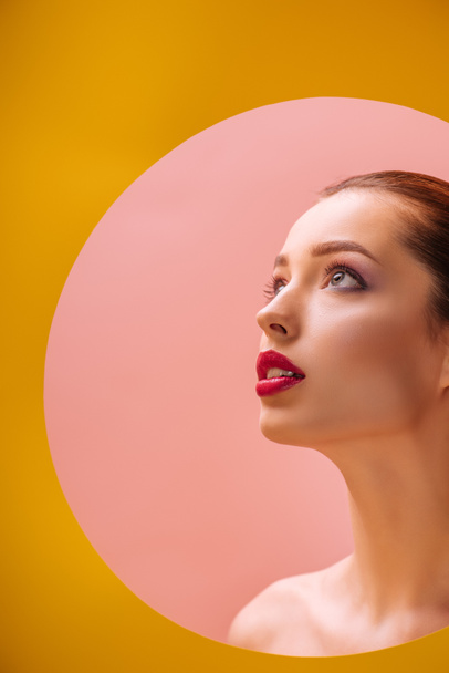 hermosa mujer desnuda con labios carmesí mirando a través de agujero círculo de papel amarillo
 - Foto, Imagen