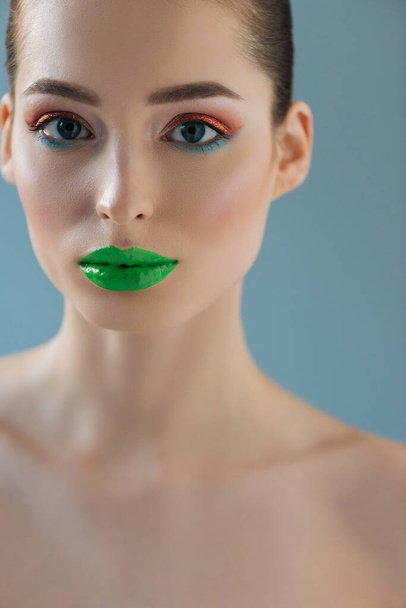 portrait of beautiful naked woman with green lips, pink and blue eyeshadow isolated on blue - Foto, Imagen