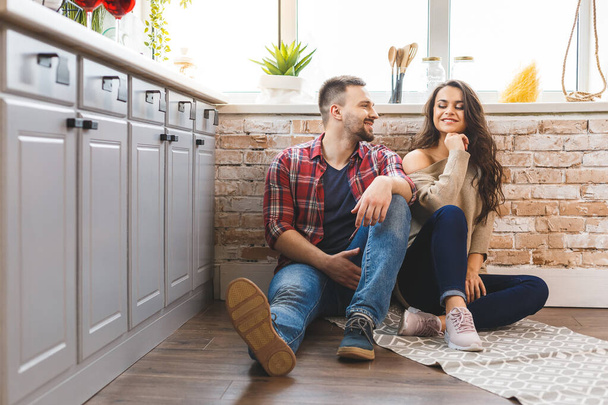 Mladý muž a žena sedí na podlaze v kuchyni a mluví. Milující mladý pár tráví čas spolu doma.  - Fotografie, Obrázek