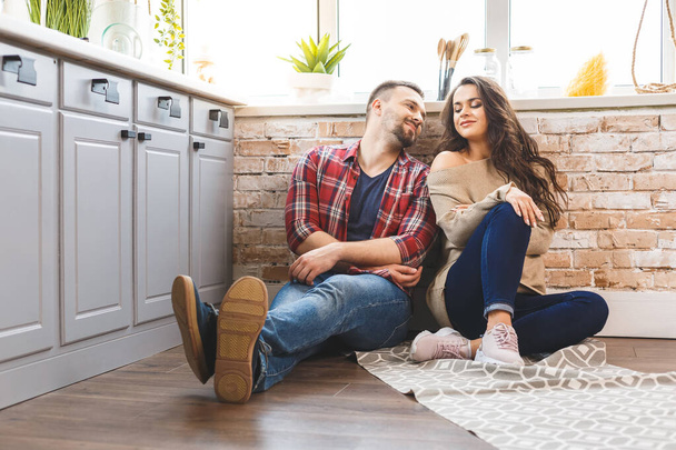 Young man and woman sitting on floor in kitchen and talking. Loving young couple spending time together at home.  - Fotoğraf, Görsel