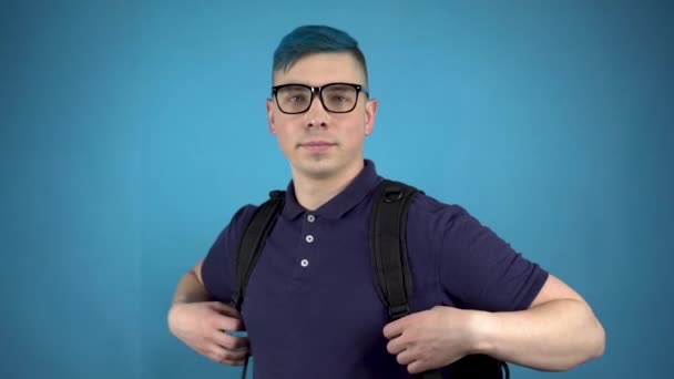 Een student met een bril met blauw haar heeft een duim. Alternatieve man met een aktetas achter zijn rug op een blauwe achtergrond. - Video