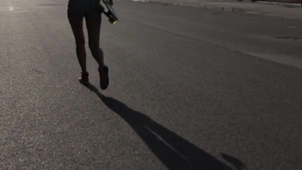 Asfalt schaduw van een meisje wandelen met skateboard in de hand op de weg. - Video