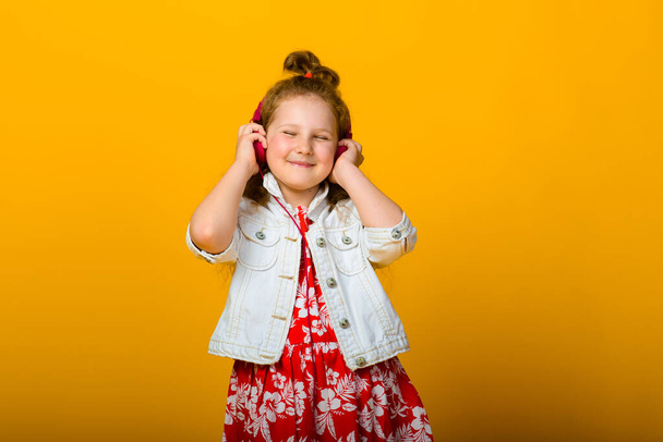 Happy carefree child emotions. Energetic joyful adorable little girl with headphones laughing at joke on yellow background in studio. - Фото, изображение