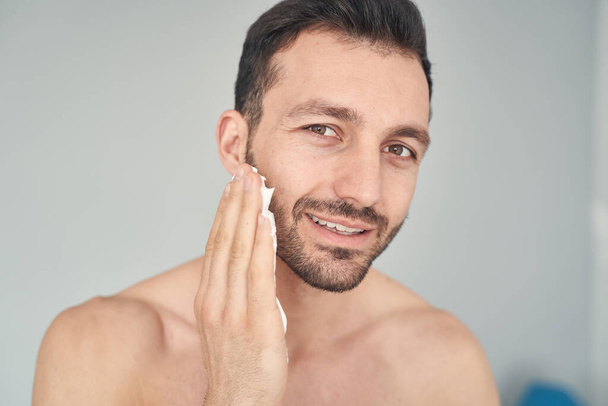 Positive young man smiling before starting shaving procedure - Foto, immagini