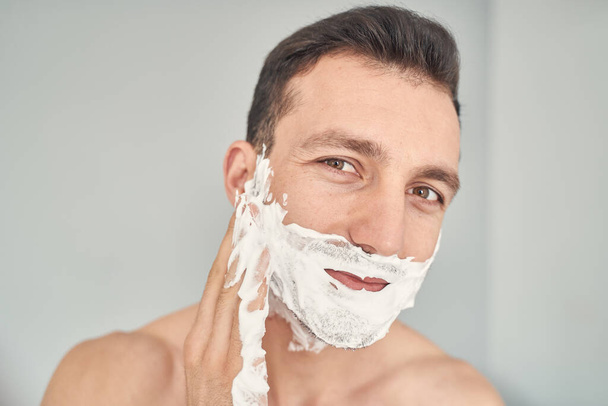 Pleasant attractive young male doing skincare routine at home - Foto, afbeelding