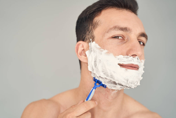 Nice-looking young man disposing of his beard and moustache - 写真・画像