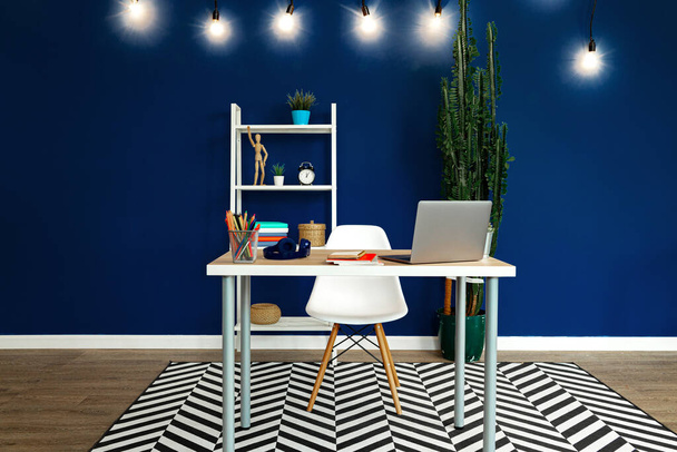 Working table with laptop against blue wall in modern flat - Φωτογραφία, εικόνα