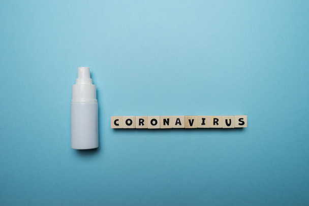Botella blanca desinfectante de manos con palabra Coronavirus escrita en bloque de madera aislado sobre fondo azul. Concepto de prevención de brotes de virus
. - Foto, imagen