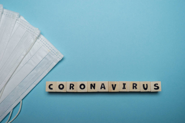 Hygiënisch gelaatsmasker met Coronavirus woord geschreven op houten blok geïsoleerd over blauwe achtergrond. Preventie van virusuitbraken. - Foto, afbeelding