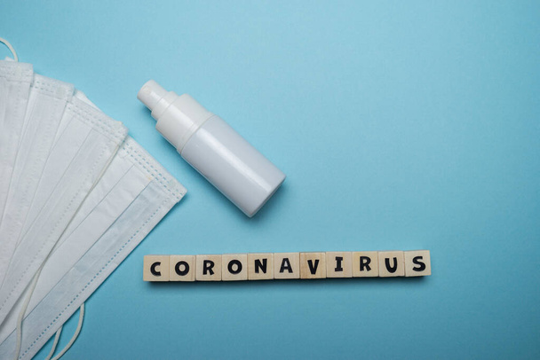 Hygienic face mask with white bottle hand sanitizer with Coronavirus word written on wood block isolated over blue background. Virus outbreak prevention concept. - Zdjęcie, obraz