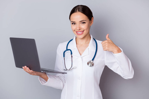 Photo of professional doc lady browsing modern technology notebook patients online video examination raise thumb up good way of communication wear lab coat isolated grey color background - Φωτογραφία, εικόνα