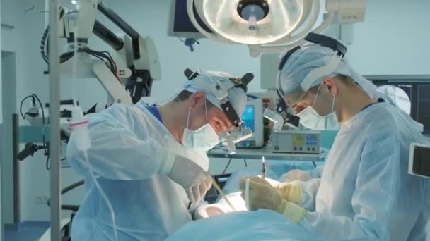 cirujanos realizan una operación y miran a través de un microscopio móvil - Metraje, vídeo