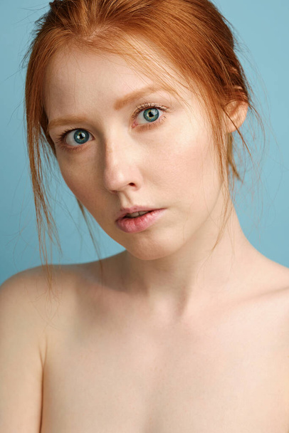 A close portrait of a red-haired girl with clean radiant skin, blue eyes and bare shoulders, looking at the camera - Foto, Imagen