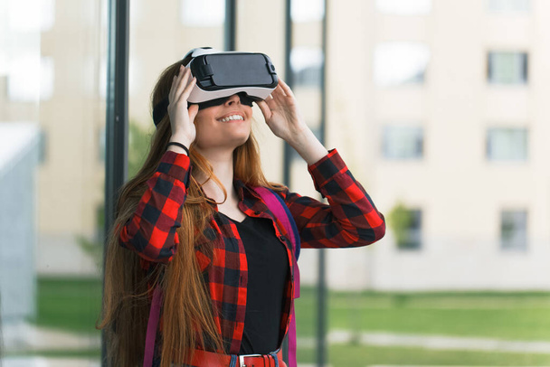 Young student plays with virtual reality glasses. Pretty girl looks at the world with 3D head mount - Photo, Image