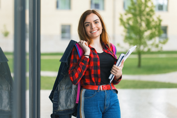 Portret van een mooie student die een jasje op zijn schouder houdt en boeken in handen heeft - Foto, afbeelding