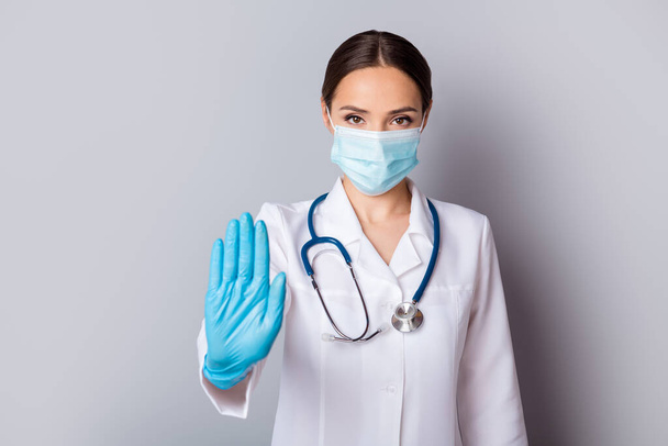 Photo of serious virologist doc lady professional hold palm stop patients stepping infected zone wear gloves facial mask medical uniform lab coat stethoscope isolated grey background - Foto, immagini