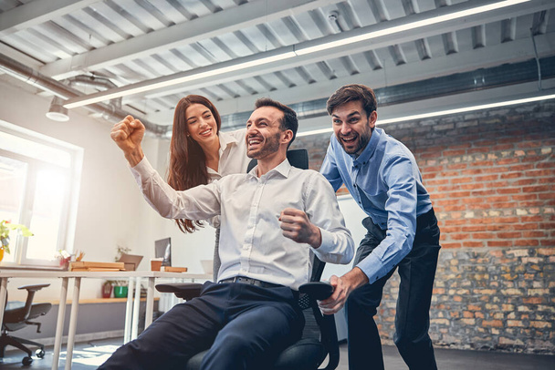 Happy co-workers racing on chairs in modern office - Fotó, kép