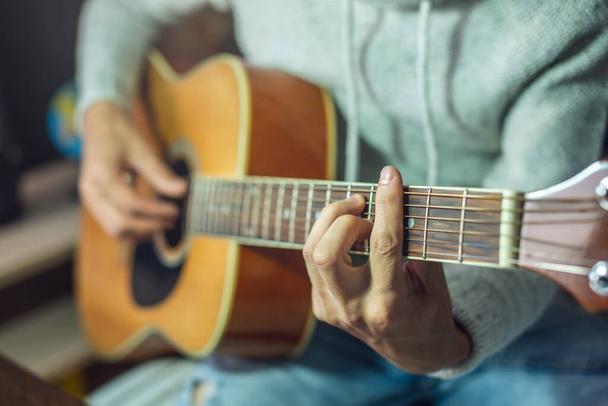 Un joven músico está aprendiendo a tocar la guitarra acústica. Un hombre toca la guitarra de cerca.
 - Foto, imagen