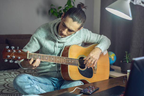 Ein junger Musiker lernt gerade, Akustikgitarre zu spielen. Ein Mann spielt eine Gitarre aus nächster Nähe - Foto, Bild