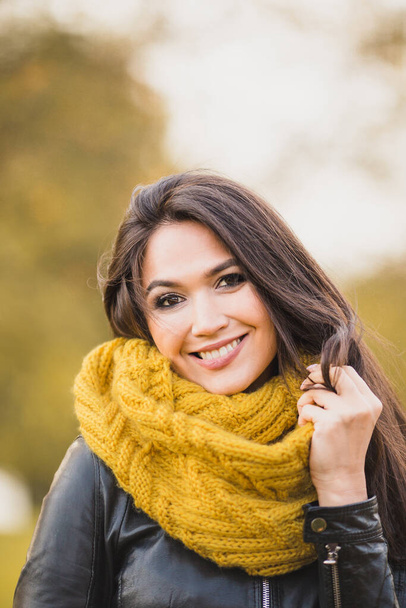 Beautiful attractive brunette girl with a charming smile in a yellow knitted scarf in autumn - Zdjęcie, obraz