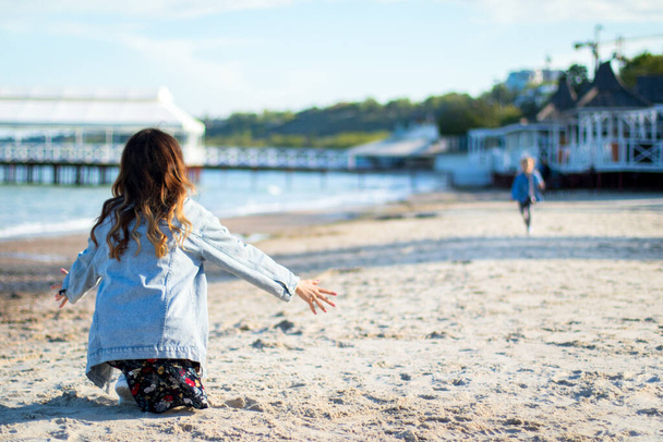 young woman in jeans jacket waiting for hugs with little girl on the beach - Photo, Image