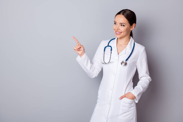 Photo of attractive family doctor doc experienced professional direct finger empty space advising vaccination center wear medical uniform lab coat stethoscope isolated grey background - 写真・画像