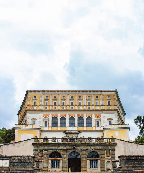 3 de junio de 2016 - Caprarola, Viterbo, Lazio, Italia - Villa Farnese. Vista de la fachada exterior del edificio, con escaleras que conducen a la entrada. Cielo azul nublado. Reloj y reloj de sol en la pared
. - Foto, imagen
