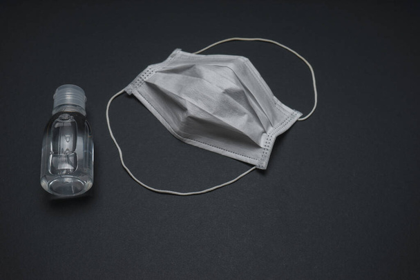 Гігієнічна маска для обличчя з чистим дезінфікуючим засобом для рук для пляшок ізольована на чорному тлі. Концепція запобігання коронавірусу
. - Фото, зображення