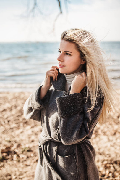 Spectacular attractive Scandinavian blonde on the shore of the Baltic Sea in autumn in a warm cozy cardigan coat - Valokuva, kuva