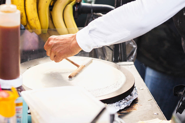 Closeup male hand bakes thin pancakes, smearing dough on a hot surface - Fotó, kép