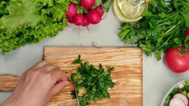 Ženské ruce s nožem sekají petržel a dávají petržel do salátu. Zavřete čerstvou zeleninu na kuchyňském stole. Žena v domácnosti vaření přírodní a zdravé jídlo na dřevěné desce - Záběry, video