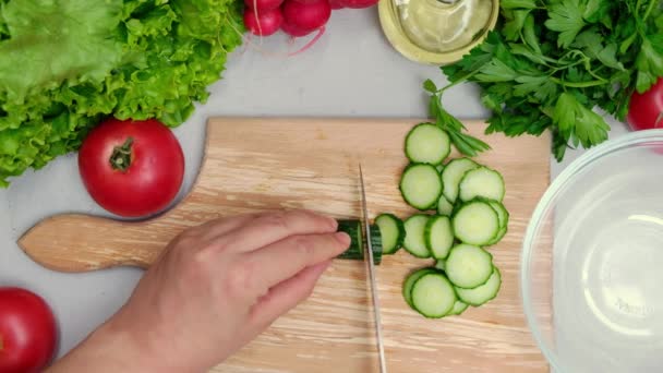 Bovenaanzicht van de vrouw die salade maakt en komkommers snijdt met keukenmes - Video
