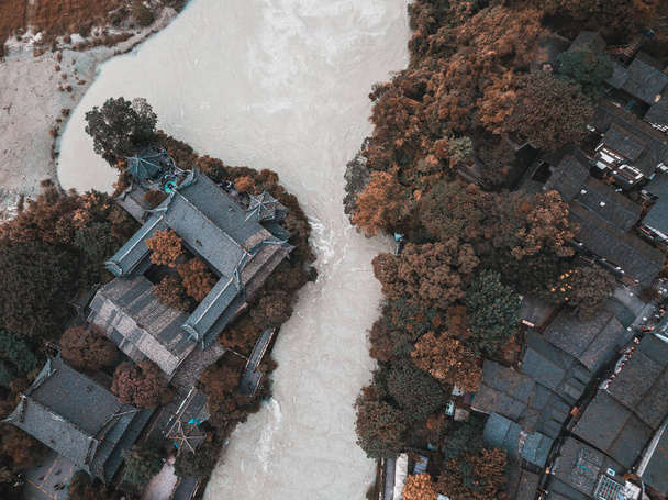 Vista aerea dall'alto verso il basso sulla parte antica della città di Dujiangyan e sistema di irregazione accanto a Chengdu, Sichuan, Cina. Vecchi edifici di architettura cinese tra gli alberi vicino al fiume Minjiang. - Foto, immagini