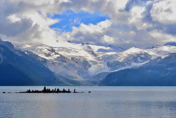 Kaunis sininen Garibaldi järvi ympäröi korkeita vuoria jäätiköillä. Salaperäinen valkoinen ja harmaa pilvet, sininen taivas. Saari, jossa on kivipyramidit.. - Valokuva, kuva