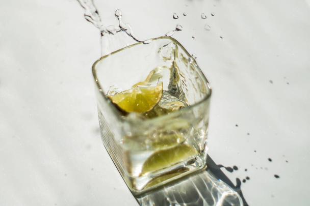 green lime fell into a glass with water on a white background - 写真・画像