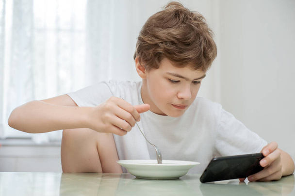 The teenager is having breakfast. Hes holding his phone while hes eating. - Foto, immagini