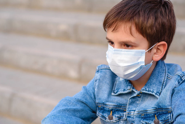 保護マスクの少年10年の階段の学校の屋外に座っている。流行性コロナウイルス2020. - 写真・画像