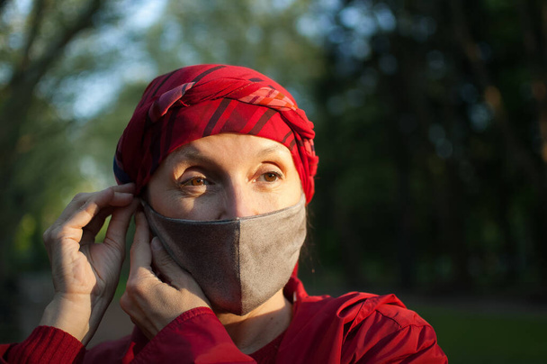Mujer madura que usa mascarilla textil hecha a mano como accesorio y elemento protector durante el soleado día de primavera en el parque debido a la pandemia de coronavirus
 - Foto, Imagen