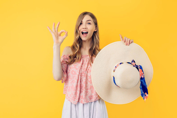 Young excited shocked woman in a summer hat, makes a good gesture, says good, confirms the information, on a yellow background - Fotografie, Obrázek