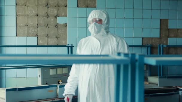 Lab technician in a protective suit and goggles approaches the table in the laboratory and begins to record data. - Materiał filmowy, wideo