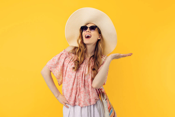 Happy young attractive woman in a summer hat and sunglasses, on an isolated yellow background - Фото, зображення