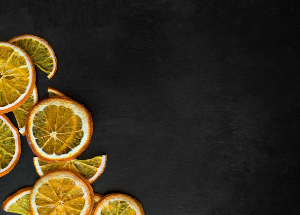 Dried orange slices on black texture. Citrus slices on the dark food background. Fruit chips flatlay - Photo, Image